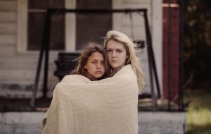 Two beautiful sad teenage girls embracing with quilt outdoors
