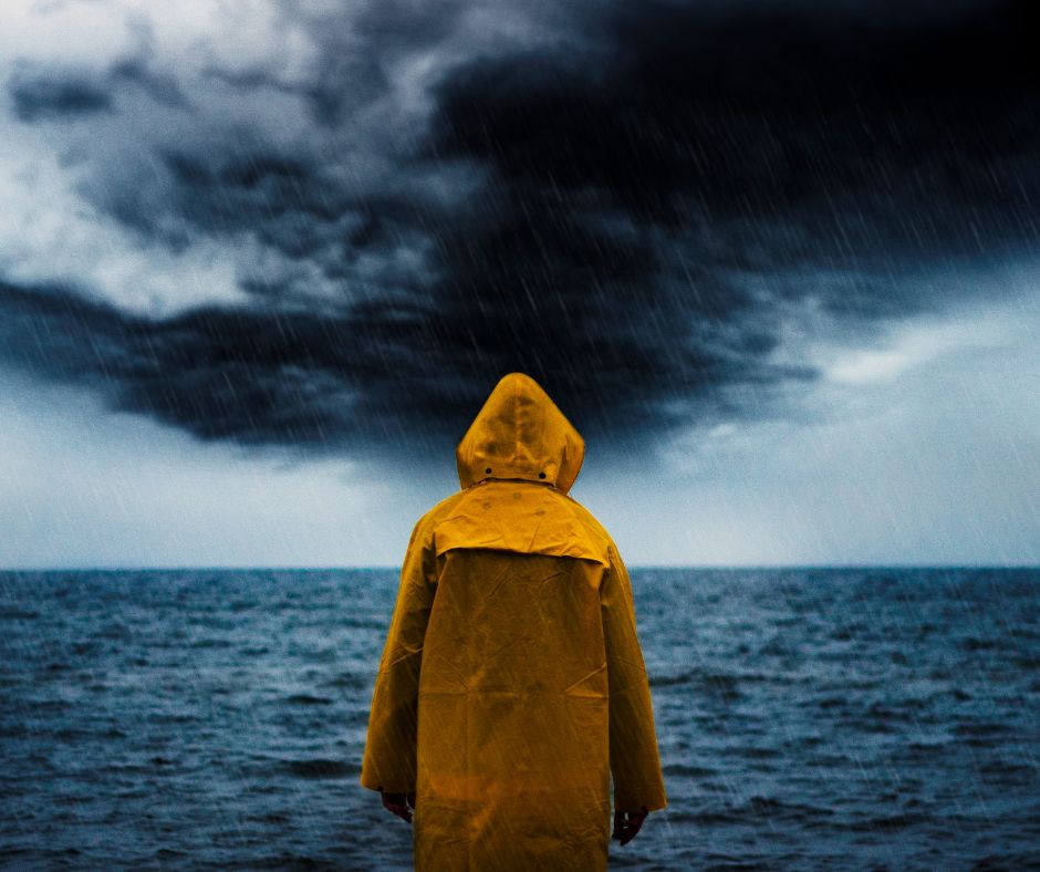 person in yellow rain coat looks over the sea with storm clouds above the horizon