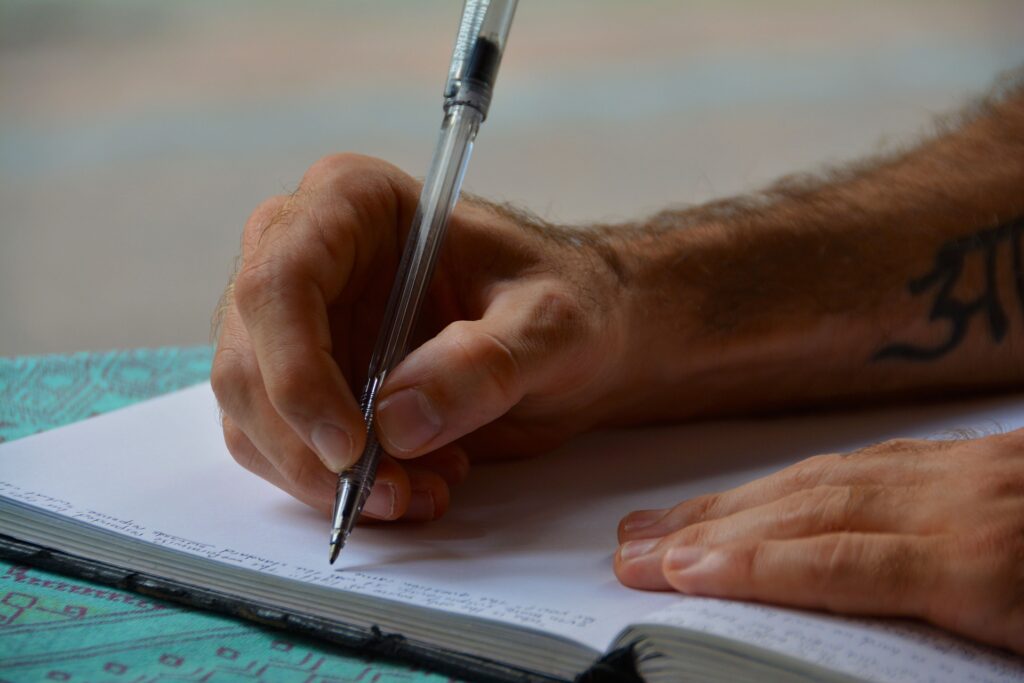 Image of a man's hands using an ink pen to write in a bound notebook.