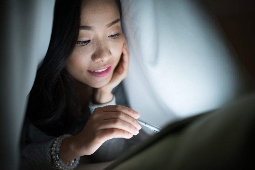 Photo of a young woman reading under the covers. 