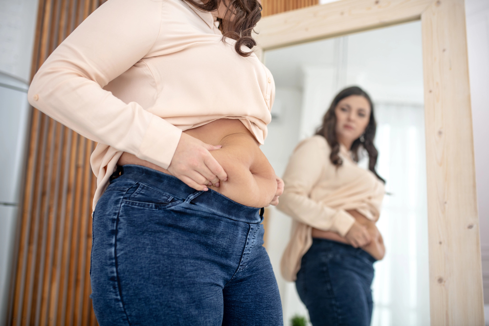 person looking in a mirror at a sagging belly