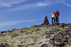 two people on top of a hill next to a cairn looking towards their next destination