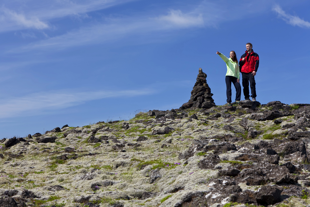 two people on top of a hill next to a cairn looking towards their next destination