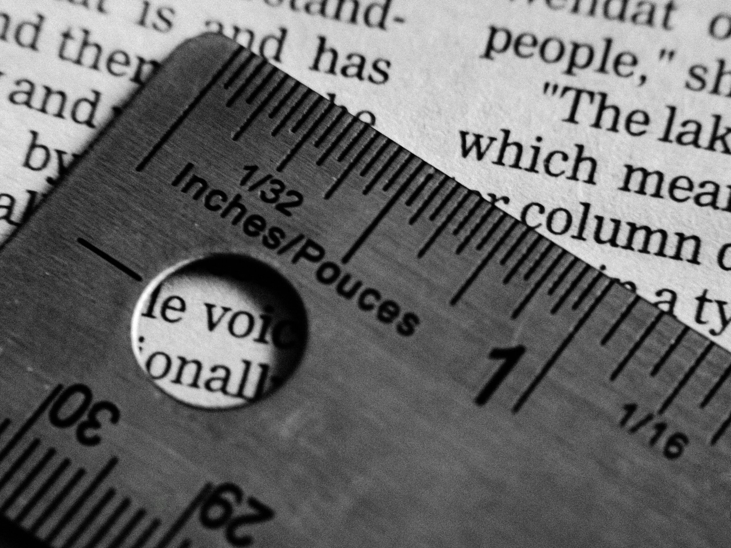 Close-up black-and-white photo of a metal ruler measuring printed words on a page, symbolizing the pressure to measure writing and being productive.